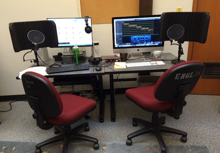 an audio recording set up with two computers, two red rolling chairs, and microphones standing on the table