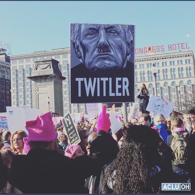 Twitler titled Trumpicon participating in a   Women’s March protest in Chicago on January 20, 2017. The person holding the poster has on a pink hat and pink gloves.
          Around this protestor are other protestors, some wearing pink hats and many holding various signs of protest.