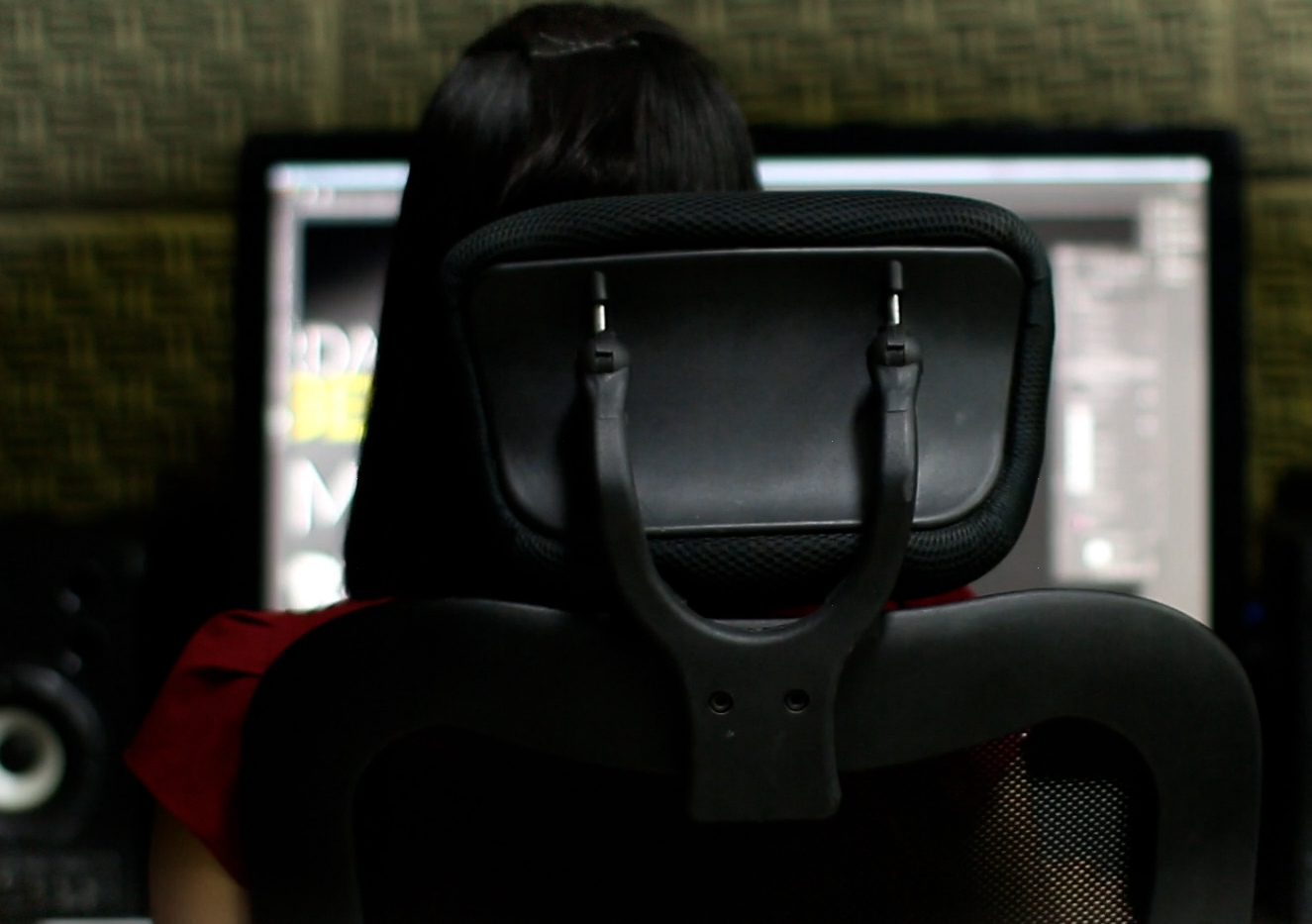 A person facing their computer and desktop speakers. Photo by Nino Souza