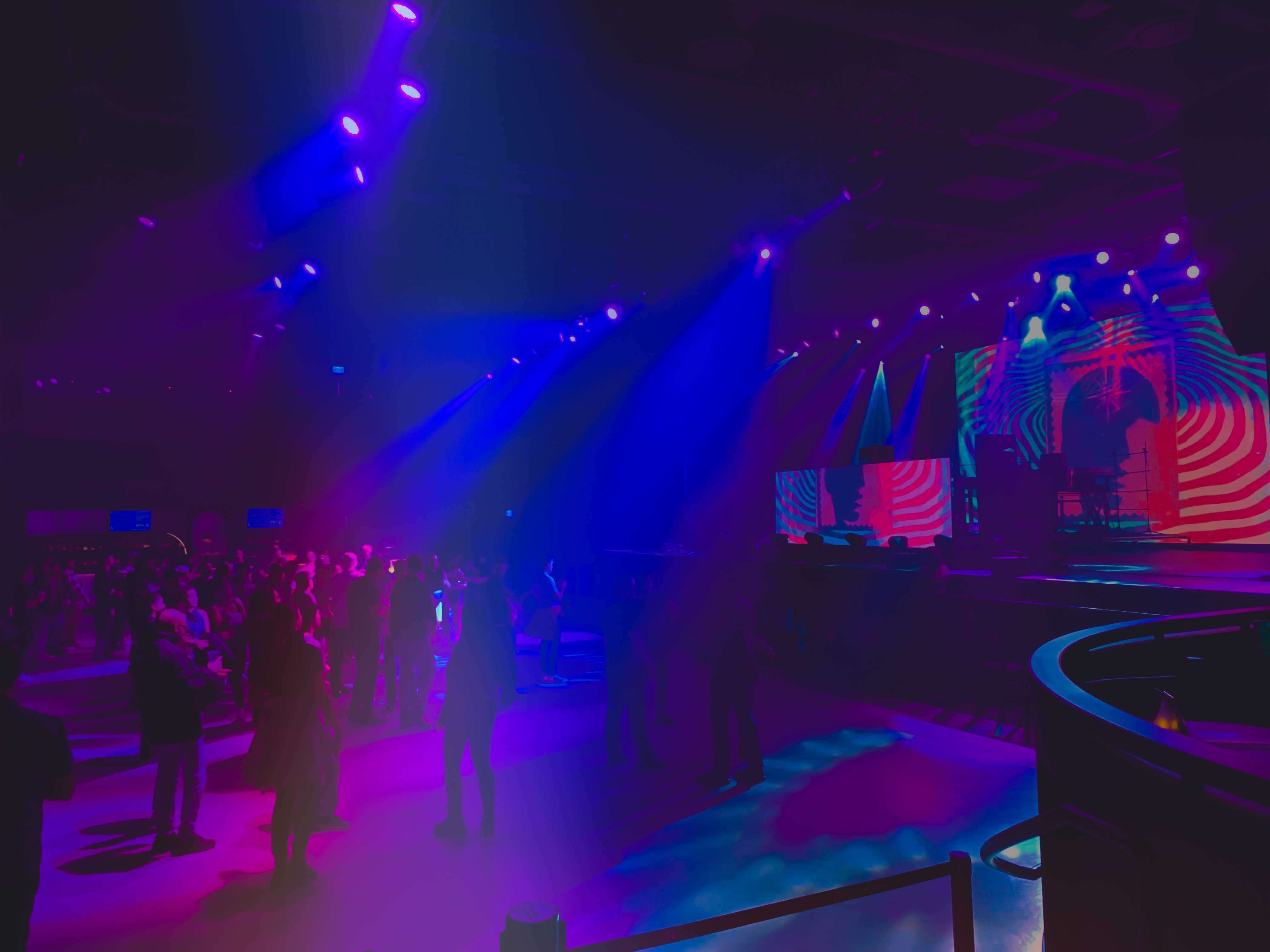 A crowd of people in a performance space that is blue and neon colors.