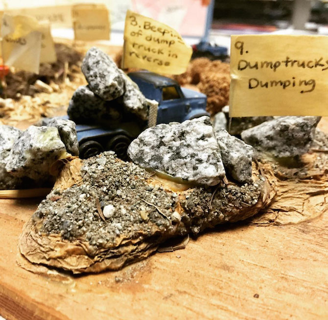 A close-up photo of a physical soundmap model, featuring several rocks and a dump truck with the note that reads, dumptrucks dumping