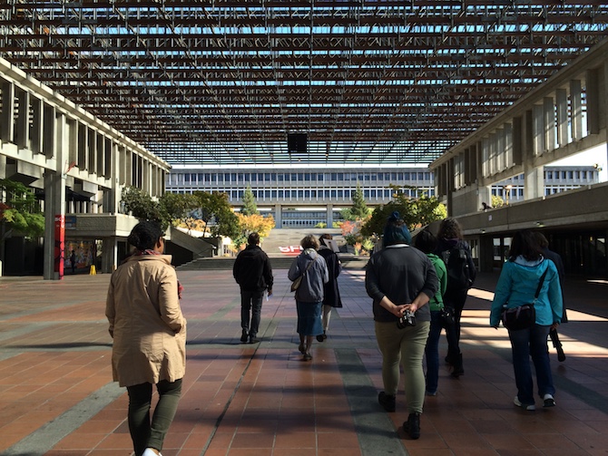 several soundwalking participants walking through SFU's convocation mall, an open space with a grid roof, part of the university campus