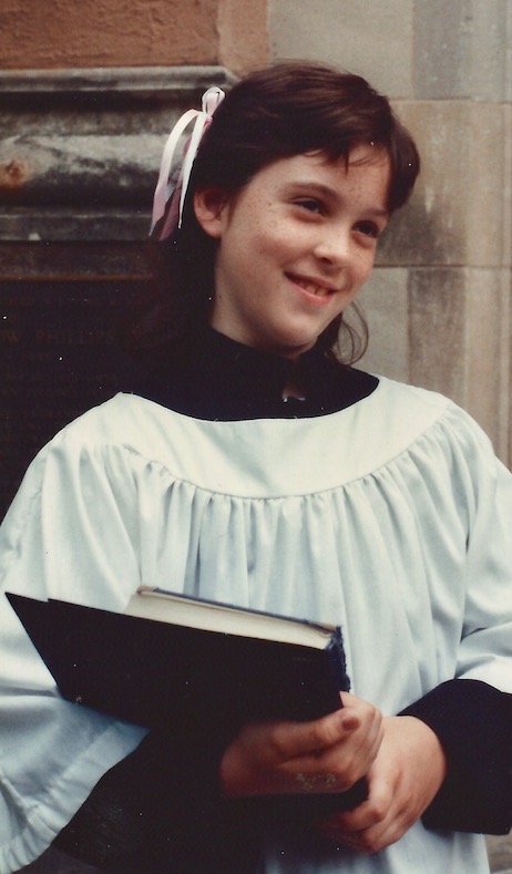 Courtney as a child standing on cathedral steps wearing choir vestments