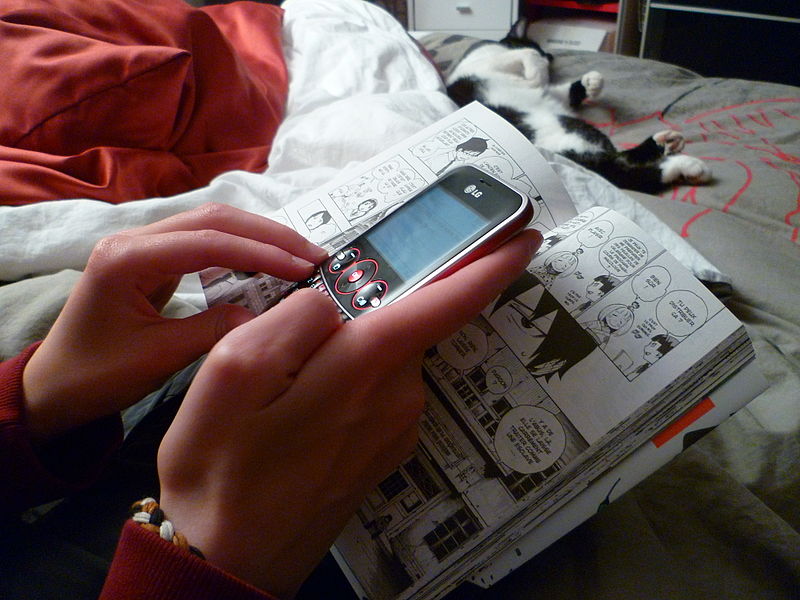 Hands of teen girl texting while reading a Manga comic