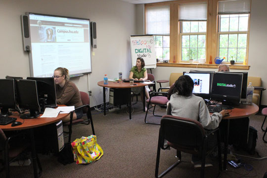 Students work with computers in a room with a Smart Board and several computer stations.