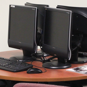 Two computer screens are on a table with one keyboard and mouse in front of the monitors. 