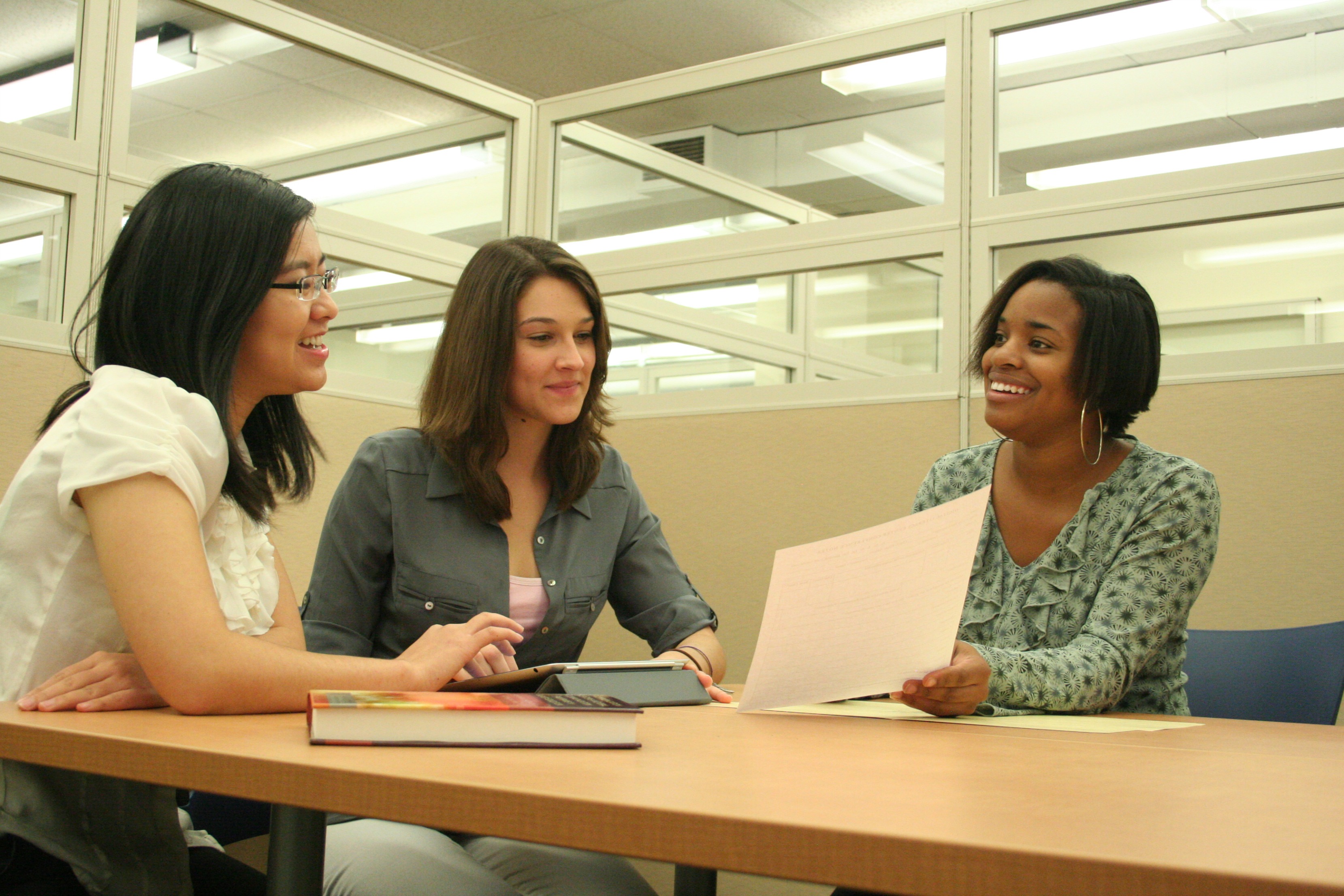 Three students look at a paper while sitting at a table.