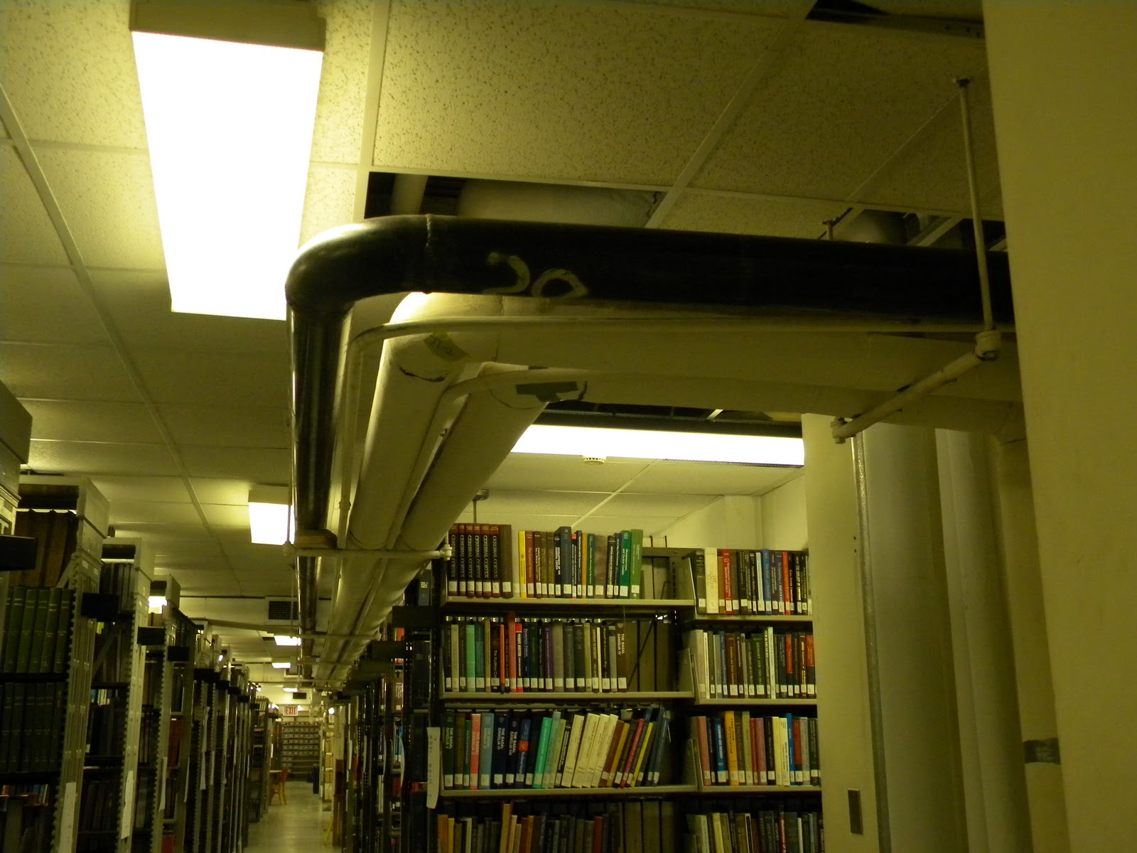 Exposed pipes run along the drop-down ceiling in a room of a library.