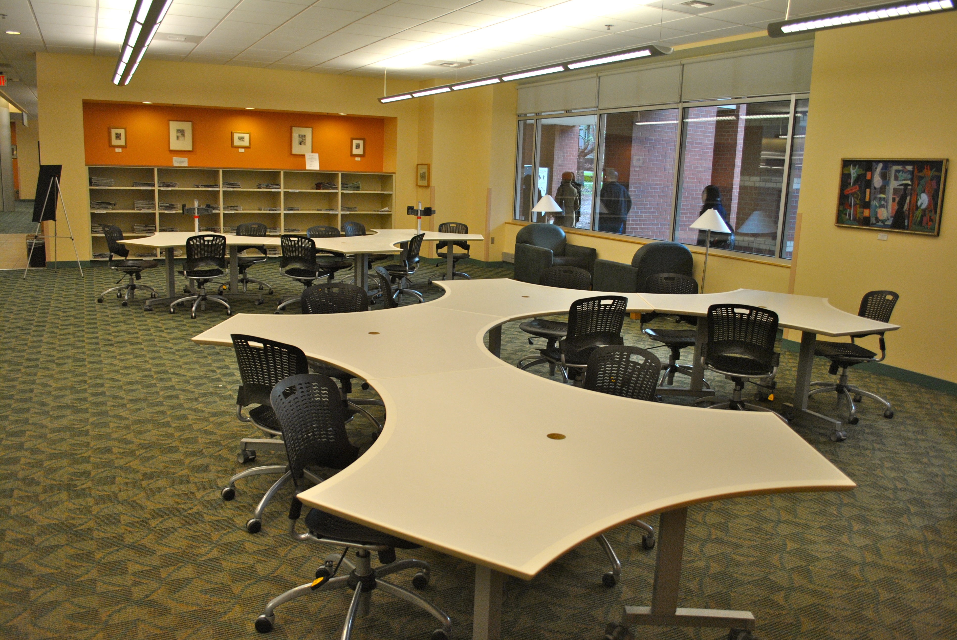 A large classroom with curved tables and chairs on wheels.