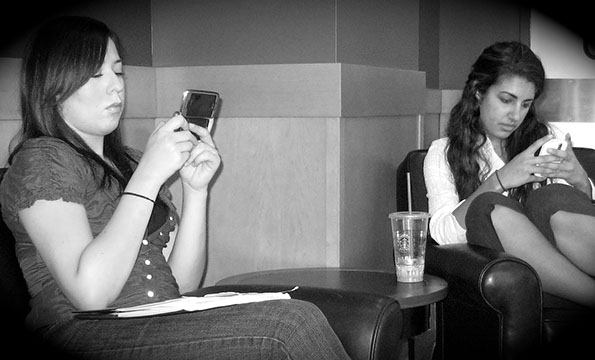Black and white photograph of two young women text messaging on their smartphones.