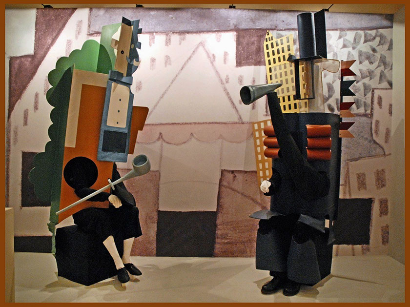 Two dancers in Picasso's costumes: the costumes are an abstract mix of formal wear, pipes, and capital/industrialist landscape.