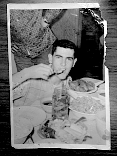 A faded and slightly torn black and white photograph of a young Glen (probably mid-20s) eating, perhaps from a jar of pickled pig's feet.