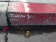 Graffiti: THANK YOU written in white on a red-painted street curb.