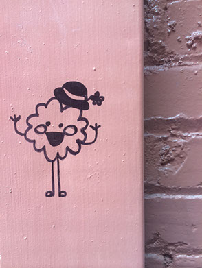 Graffiti: An odd figure painted on a fusebox. The figure looks like a cross between a puffball and a leprechaun with a bowler hat.