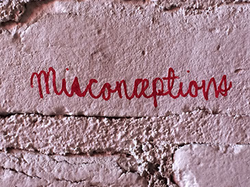 Graffiti: "Misconceptions" written in red cursive on a pale pink brick wall.