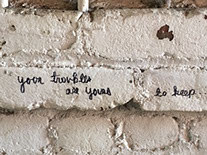 Graffiti: "Your troubles are yours to keep" written in black cursive on a white brick wall.