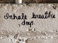 Graffiti: "Inhale breathe deep" written in black cursive on a white brick wall.