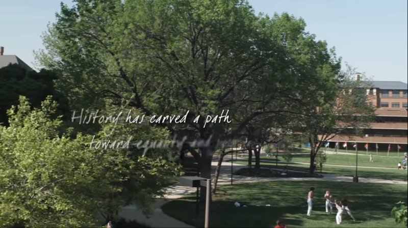 An overview shot of Gallaudet campus in the daytime with trees, grass, and a building in the background. Words are handwritten across the campus reading, "History has carved a path toward" with the next few words blurred as they appear on screen.