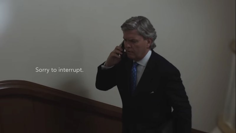 A man walks up a staircase talking on a cell phone as white captions appear to his right: "Sorry to interrupt."