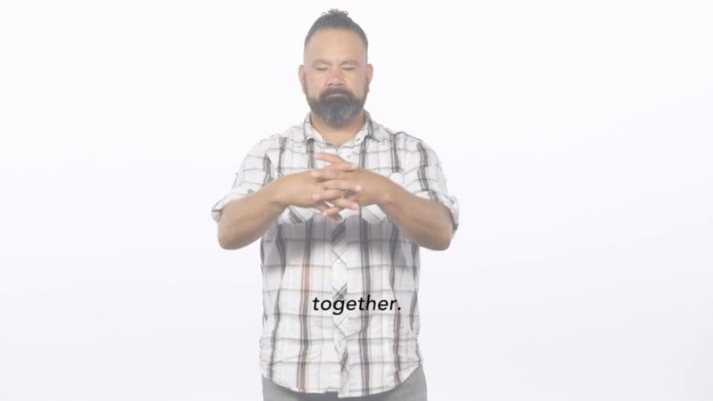 Paco, standing in front of a white background, signs to the camera as he directly faces the camera and signs the word "together." Open subtitles appear in front of him. The subtitles read, "together."