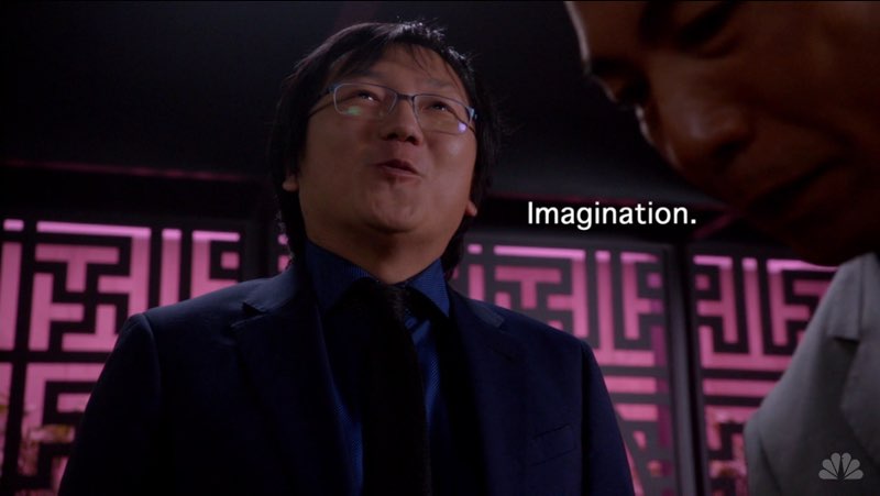 A male Japanese character looks up, a pink-and-black maze-like wall in the background, slightly smiling. White subtitles appear to his left reading, "Imagination."