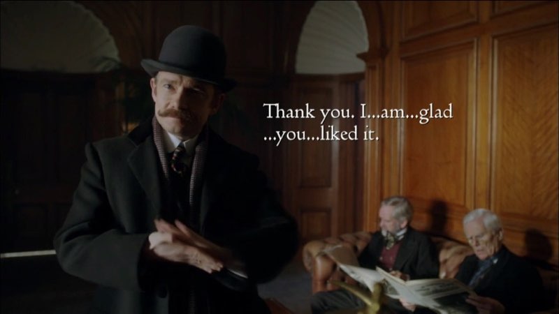 Watson is dressed in Victorian-era clothes and attempting to sign. Open subtitles appear on the right side of the screen near his face. They read, “Thank you. I…am…glad… you… liked it.”