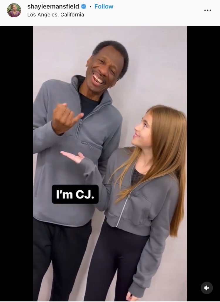 This screenshot of Shaylee’s Instagram post shows Shaylee and CJ, both wearing gray tops and black pants, standing as they smile. Shaylee is gesturing to CJ and CJ is signing the letter "J." Open subtitles appear in front of him and read, "I'm CJ."