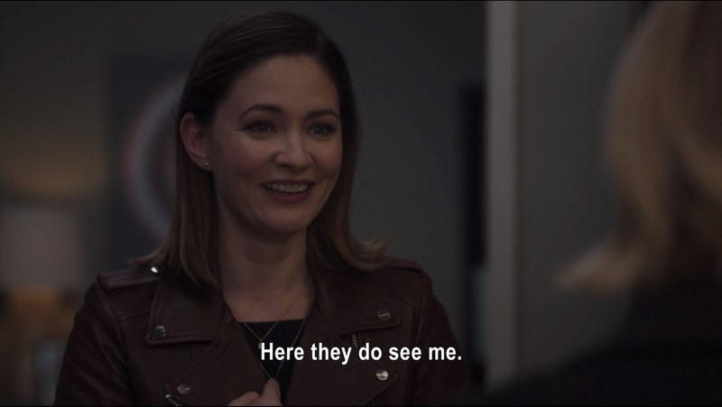 Elizabeth, in regular clothes, is smiling. Subtitles at the bottom read, "Here they do see me."