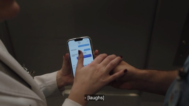 Two characters both hold a phone and each other's hands. The phone screen shows an iPhone text message conversation. Closed captions at the bottom state, "- [laughs]."