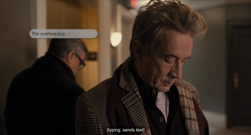 Oliver is looking down as he types on his phone, although his phone is not visible. A text message bubble appears near his face, reading, "The overture is p..." Closed captions at the bottom of the screen read, "[typing, sends text]."