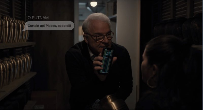 Charles is showing his phone to Mabel. A text message bubble appears next to his face. The message is from Oliver. Putnam and reads, "Curtain up! Places, people!!!!"