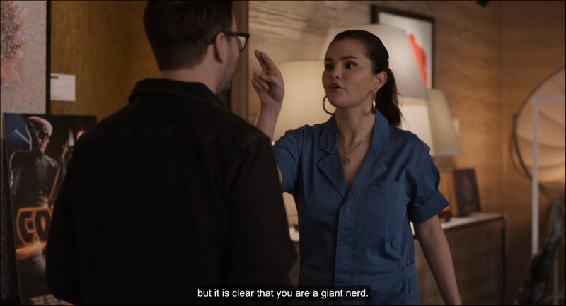 Mabel stands in front of Theo while moving her hand to his face. She is speaking and signing. Closed captions appear at the bottom stating, “but it is clear that you are a giant nerd.”