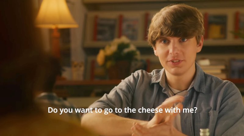 A male student is in a library signing, “cheese.” Subtitles at the bottom read, "Do you want to go to the cheese with me?"