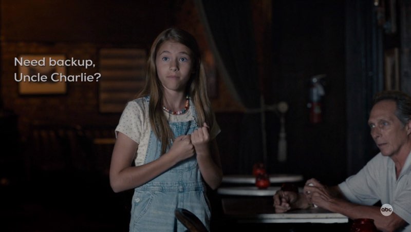 Ollie is standing next to the seated Leo, her eyes directed at Charlie, who is off-camera. She signs with open subtitles next to her, "Need backup, Uncle Charlie?"