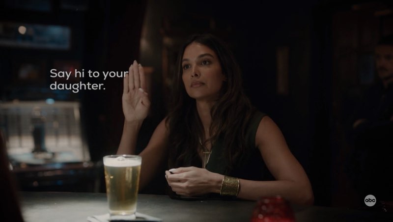 Daphne is seated at a bar, looking serious as she signs “Hi.” Open subtitles appear next to her hands that read, "Say hi to your daughter."