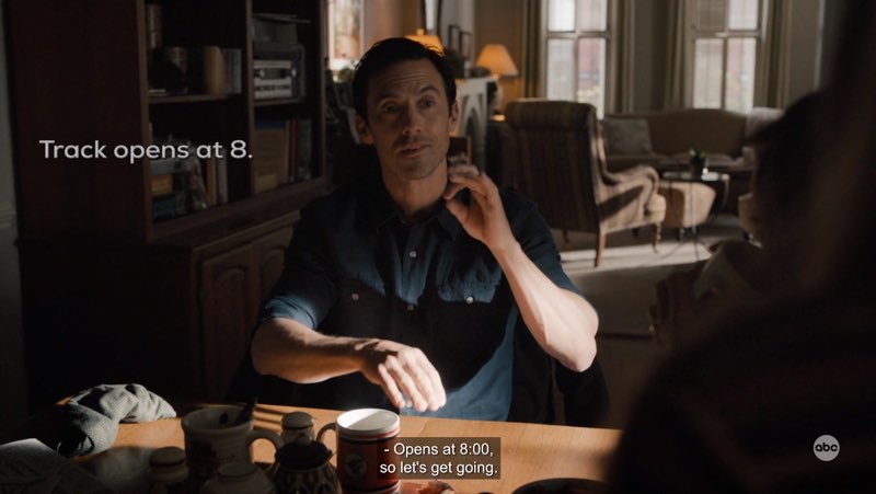 Charlie is seated at the dining table and signing the word “eight.” Open subtitles appear next to him that read, "Track opens at 8." Closed captions at the bottom read "Opens at 8:00, so let's get going."