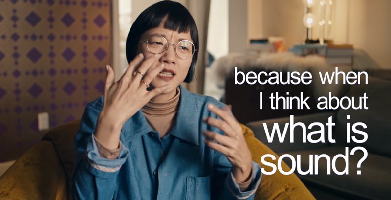 Christine Sun Kim is seated as she signs. Lowercase open captions appear on the right side: “because when I think about what is sound?” The last three words are larger than the others for emphasis.